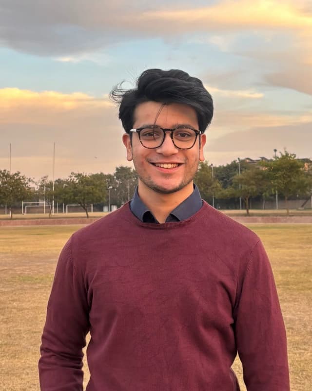 Hammad Javaid, smiling, in a maroon sweater, outdoors at sunset